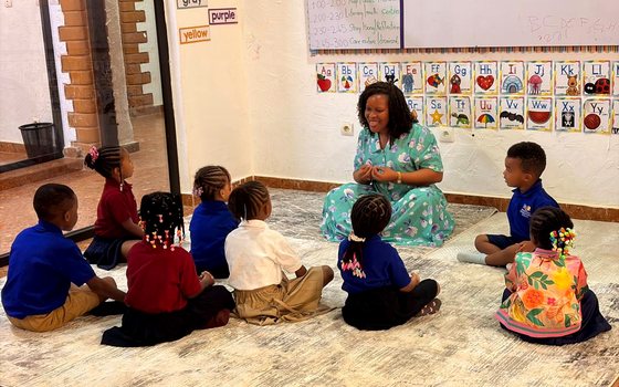 A teacher leads circle time with a group of young students seated on a rug in a bright classroom