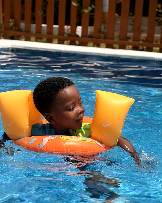 A young student floating in the pool with orange armbands