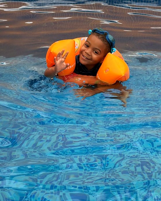 A smiling student in goggles and armbands waving from the pool
